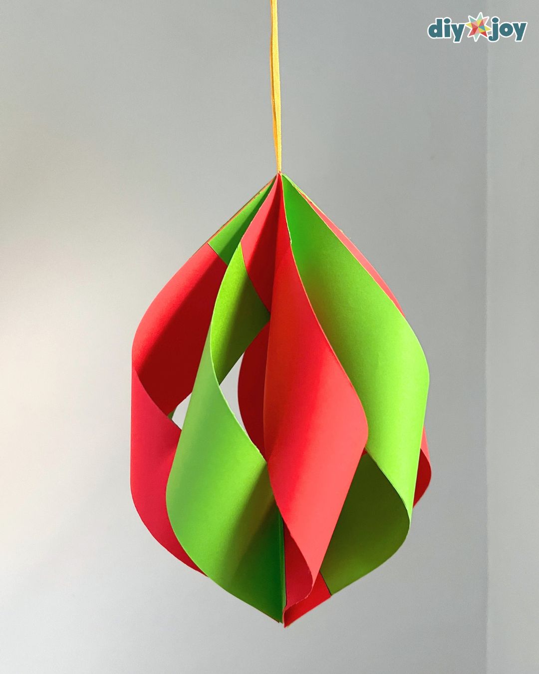 One large red and green folded paper ornament on a gold ribbon, showing the twisted strips of this DIY Christmas decor