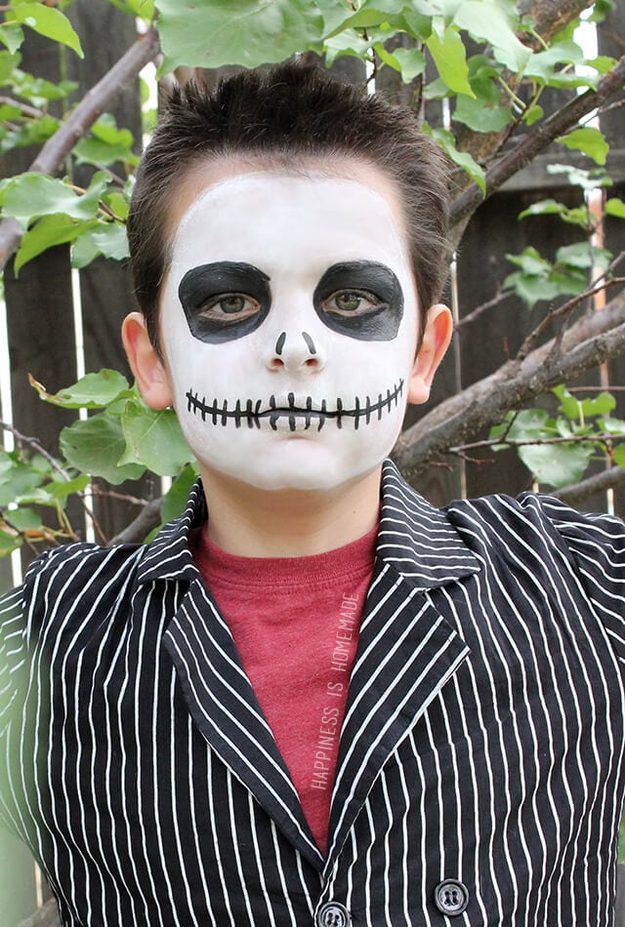 Jack Skellington Halloween makeup on a boy with white face paint, black sunken eyes and a stitched grin