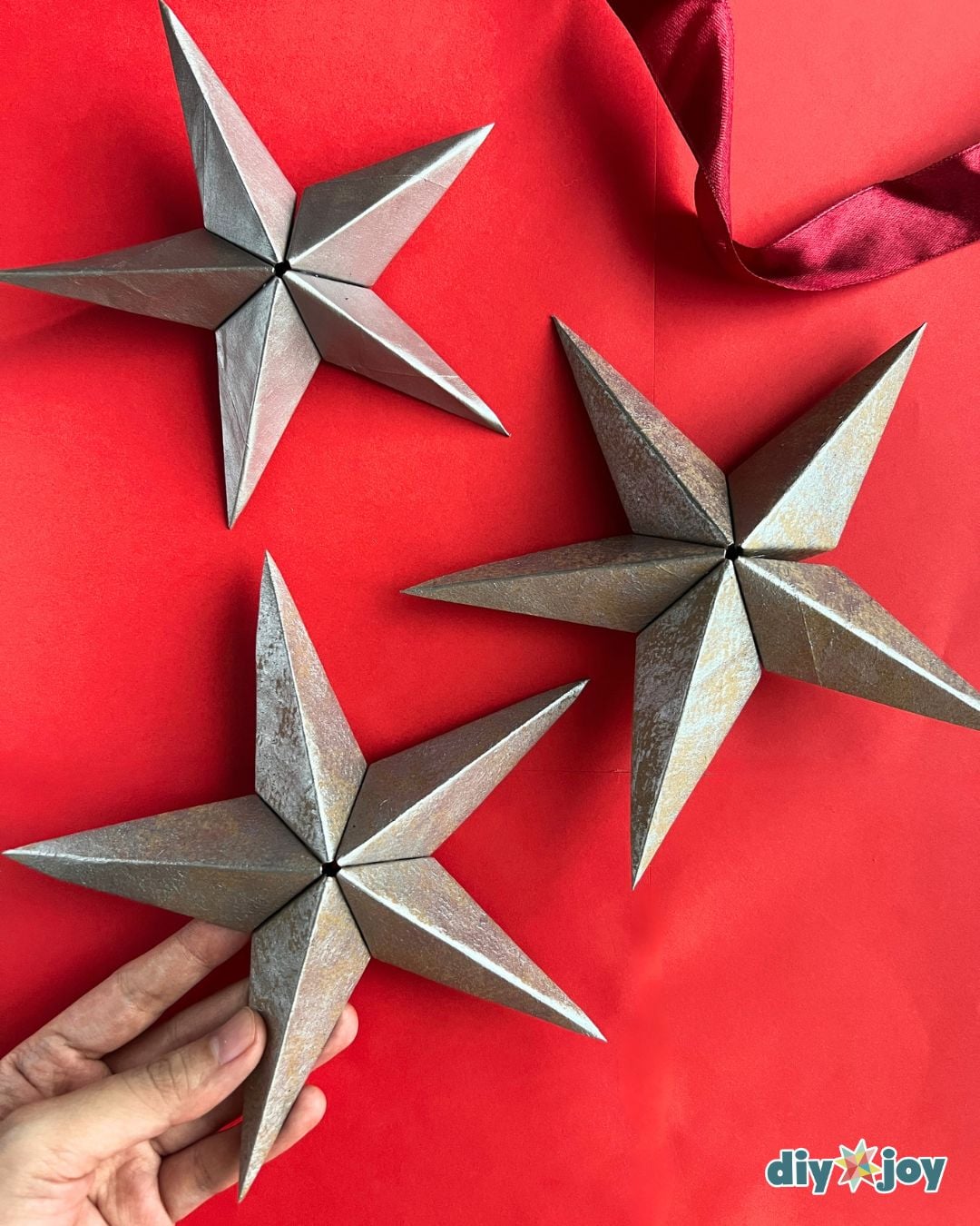 Silver paper star ornaments - three finished DIY Christmas stars on a red background, homemade decor