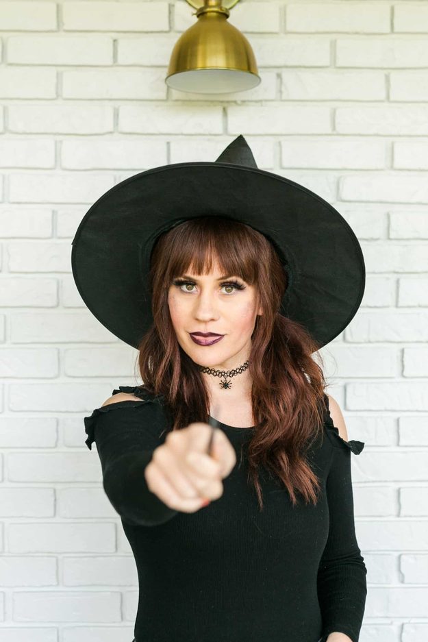 Witch Halloween makeup with smoky purple eyes, dark plum lips, a black hat, spider choker and a black wand