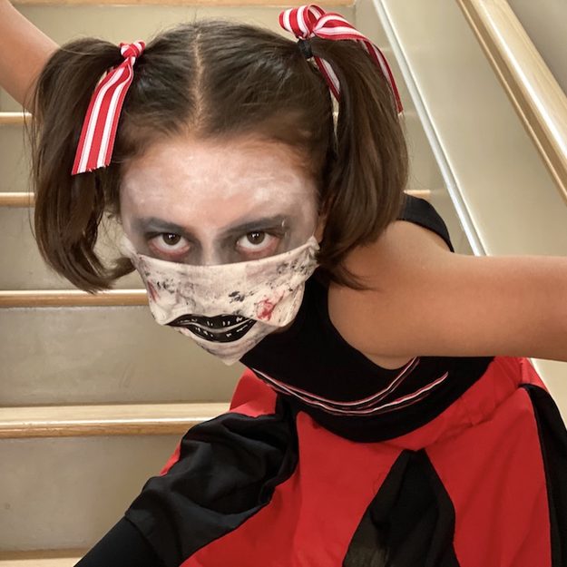 Zombie cheerleader Halloween makeup with dark eyes, pale skin and a painted fabric mask over the mouth