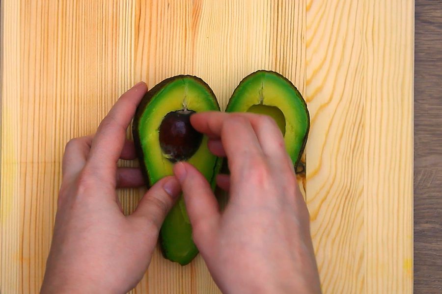 Twisting a halved avocado apart on a wooden board