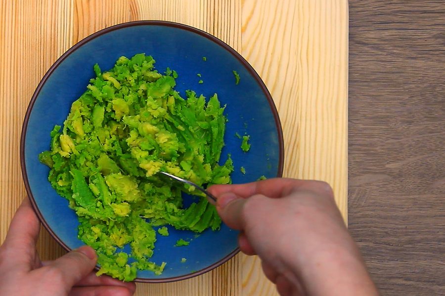 Mashing avocado with salt in a blue bowl