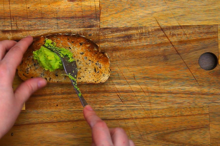 Spreading mashed avocado over the toasted bread with a knife