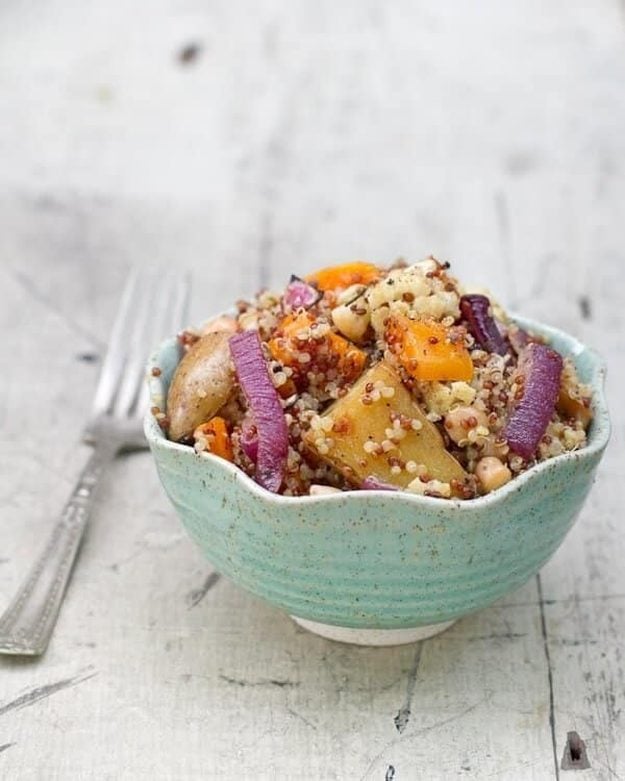 Roasted Harvest Vegetables With Quinoa Bowl Quinoa with roasted fingerling potatoes, squash, cauliflower and chickpeas in a turquoise scalloped bowl, white wood