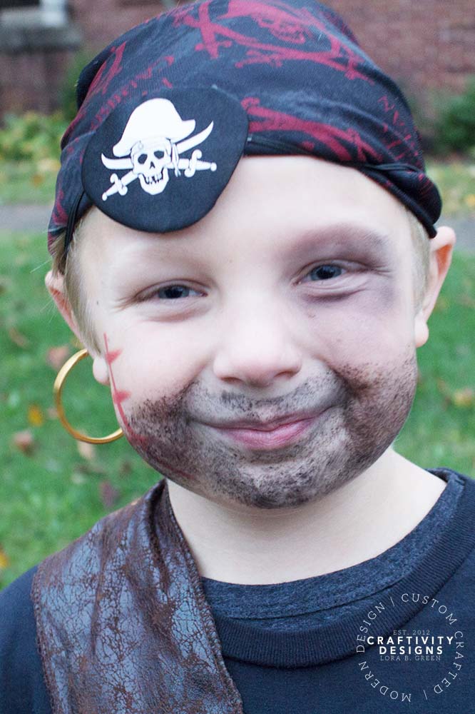 DIY pirate Halloween makeup on a child with a painted beard and mustache, cheek scar and black eye patch