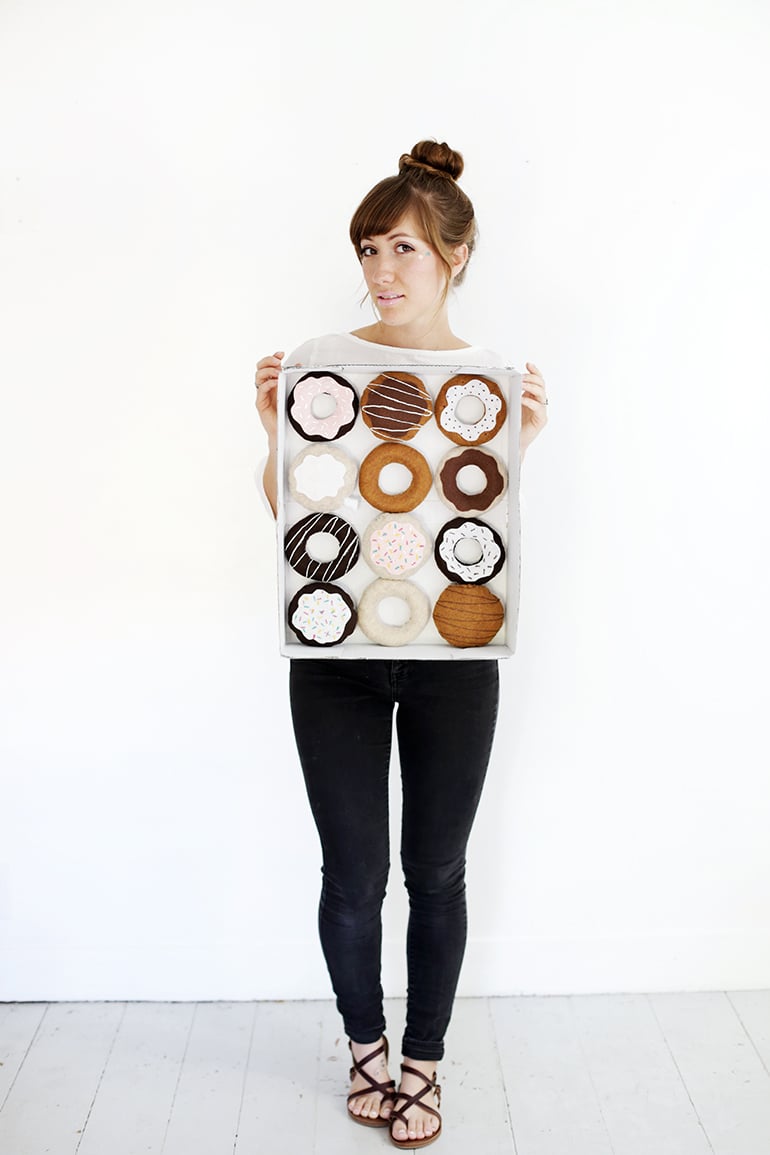 DIY Dozen Donuts Halloween Costume Adult wearing a DIY donut costume with twelve felt donuts arranged inside a painted cardboard bakery box