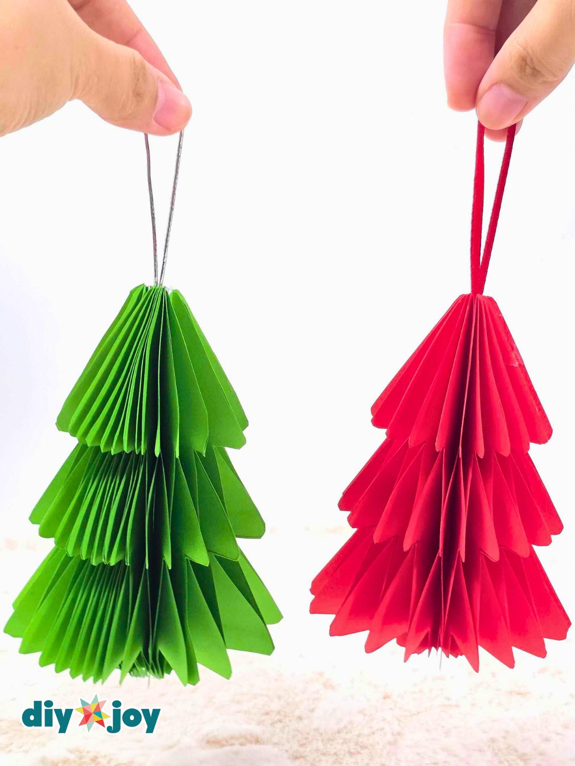 Honeycomb Paper Christmas Tree Ornaments Green and red honeycomb paper Christmas trees with ribbon hanging loops held up against a white background