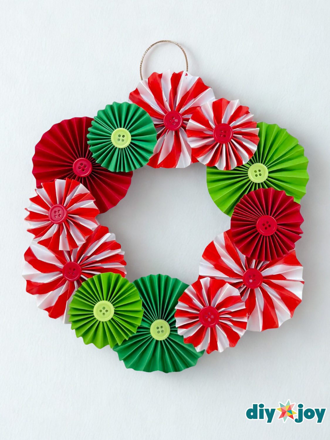 Paper Rosette Christmas Wreath Christmas paper wreath made of red, green and peppermint striped accordion rosettes with button centers on a white wall