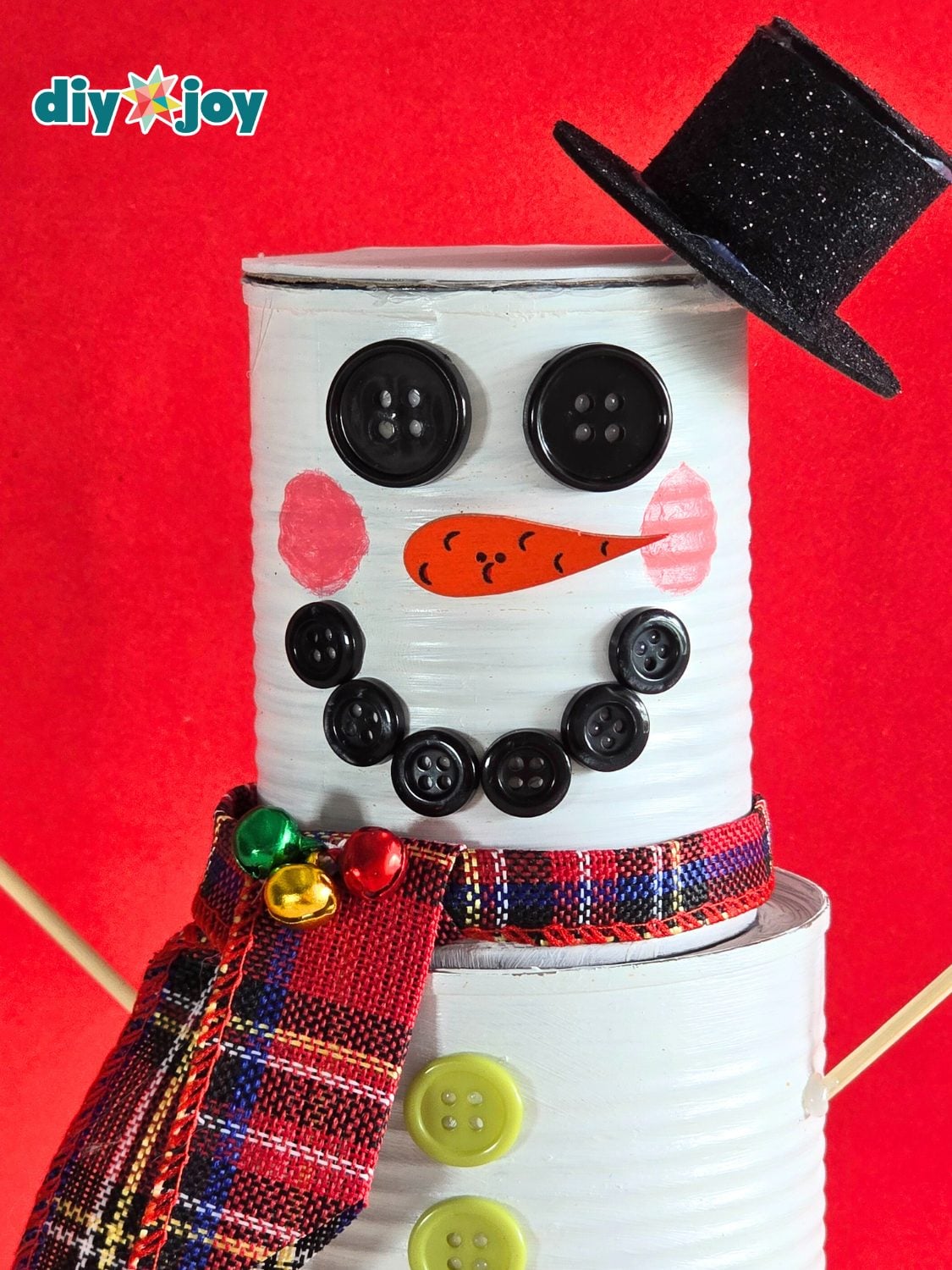 Tin Can Snowman From Recycled Cans Tin can snowman with button eyes and smile, an orange carrot nose, a plaid ribbon scarf with bells and a glitter foam top hat