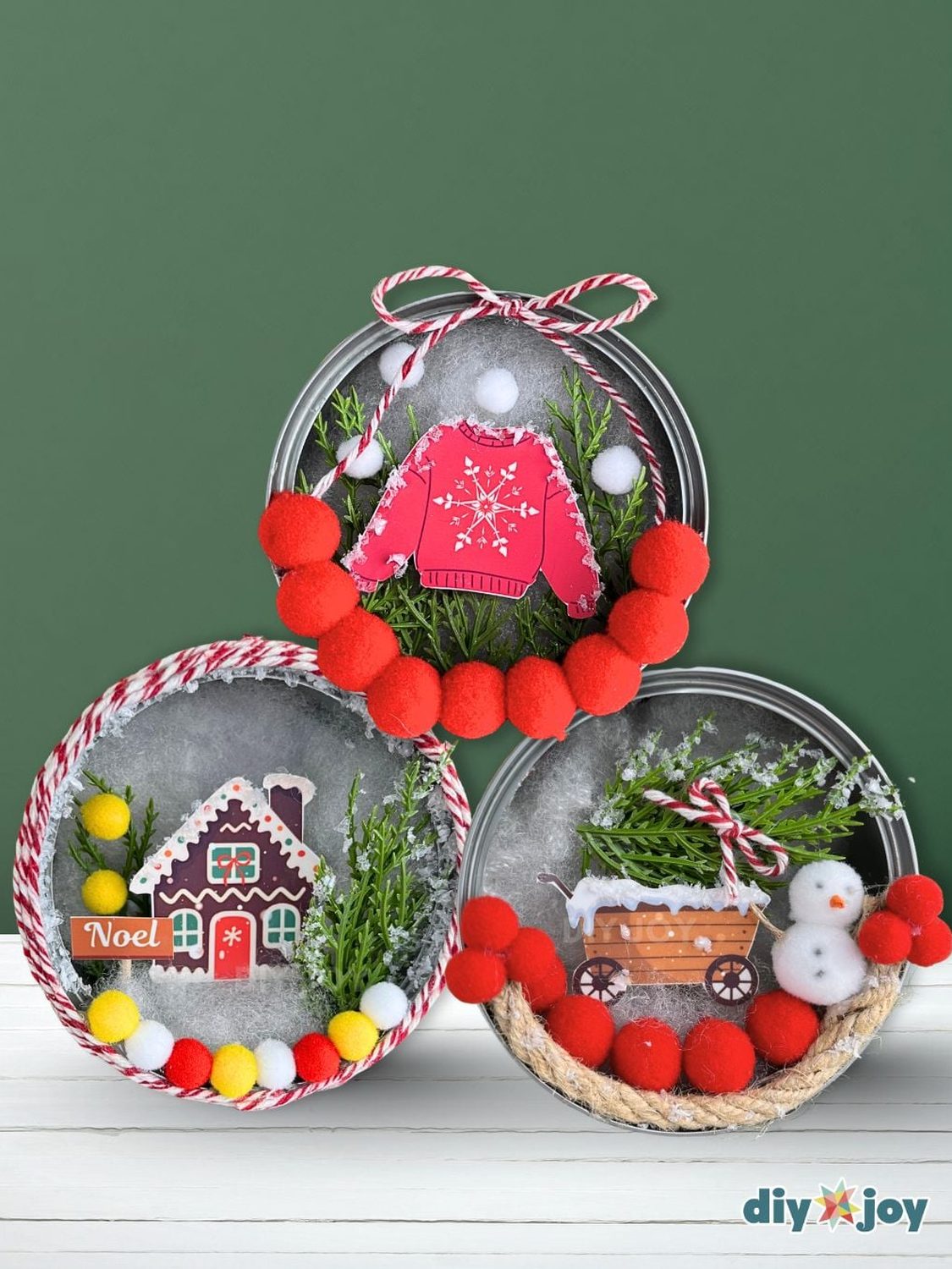 Tuna Can Shadow Box Ornament Trio Three tuna can shadow box ornaments with a red sweater, a gingerbread house and a snowman scene, trimmed with pom poms