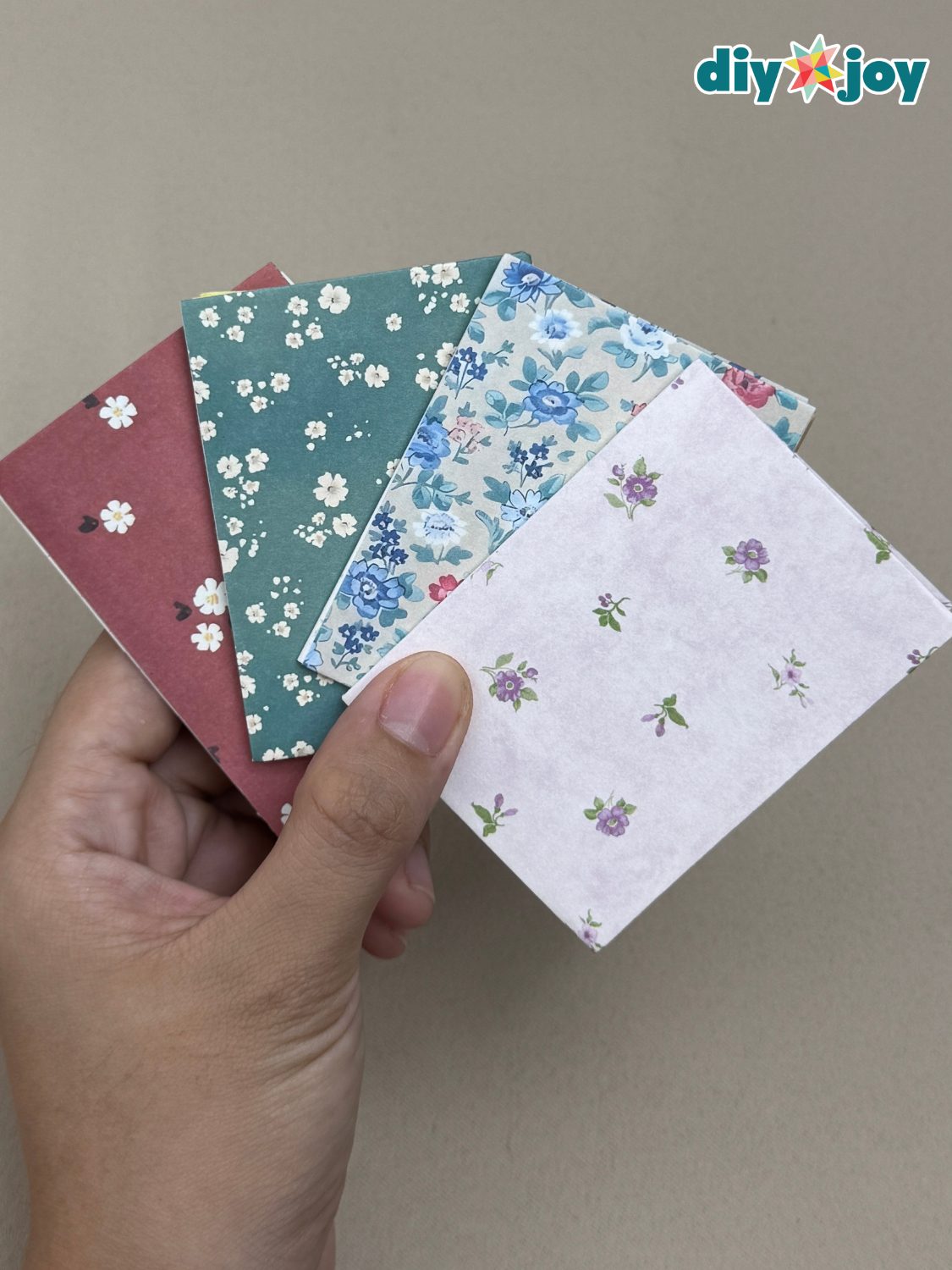 Small handmade notebooks with floral and solid cardstock covers held in one hand, one open to yellow accordion pages