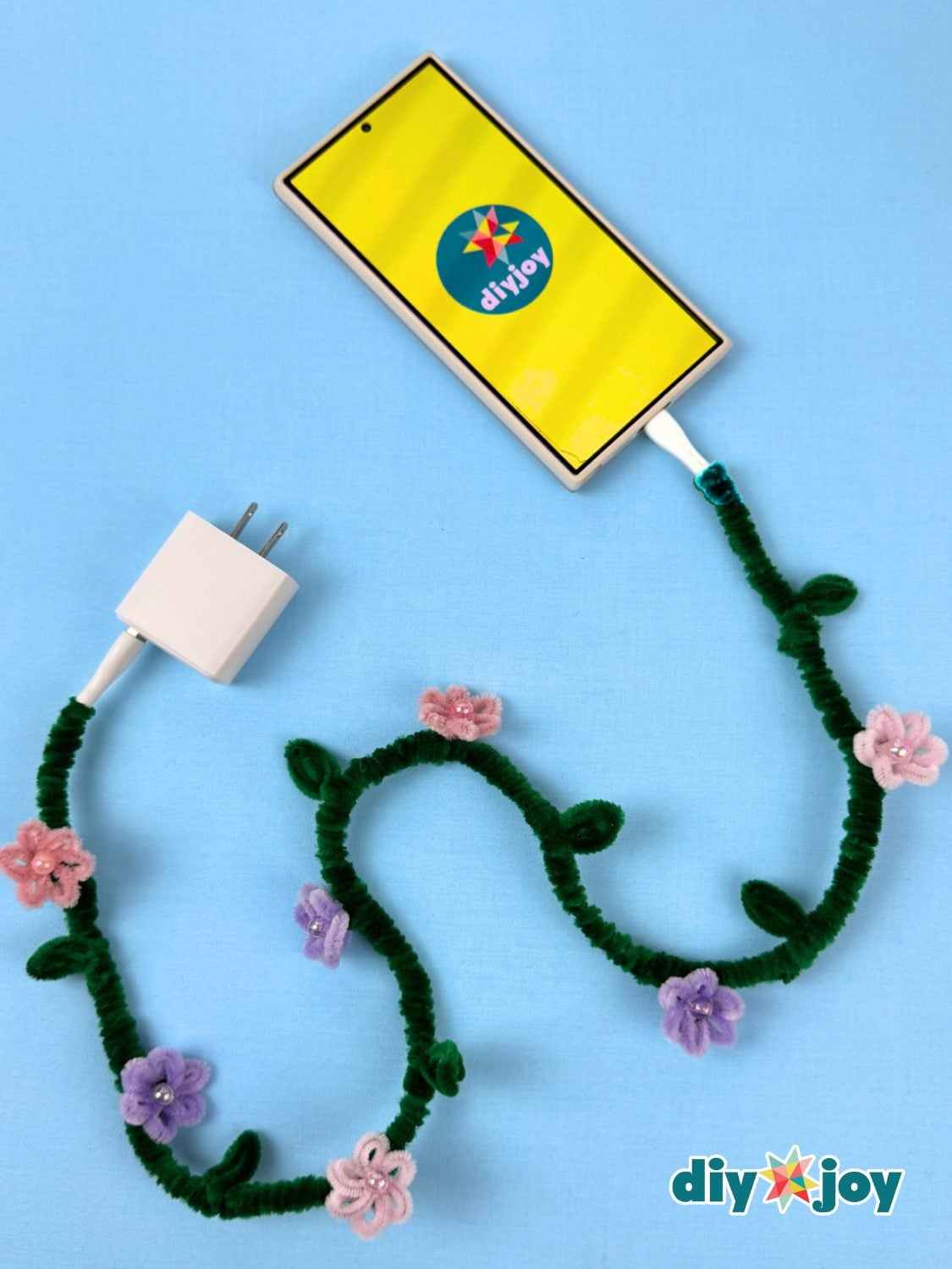 White charger cable wrapped in a green pipe cleaner vine with small twisted leaves running along its length