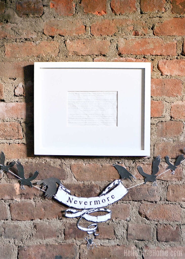 Framed Raven poem above a black-and-white Nevermore bird banner on a brick wall with Hello Little Home watermark