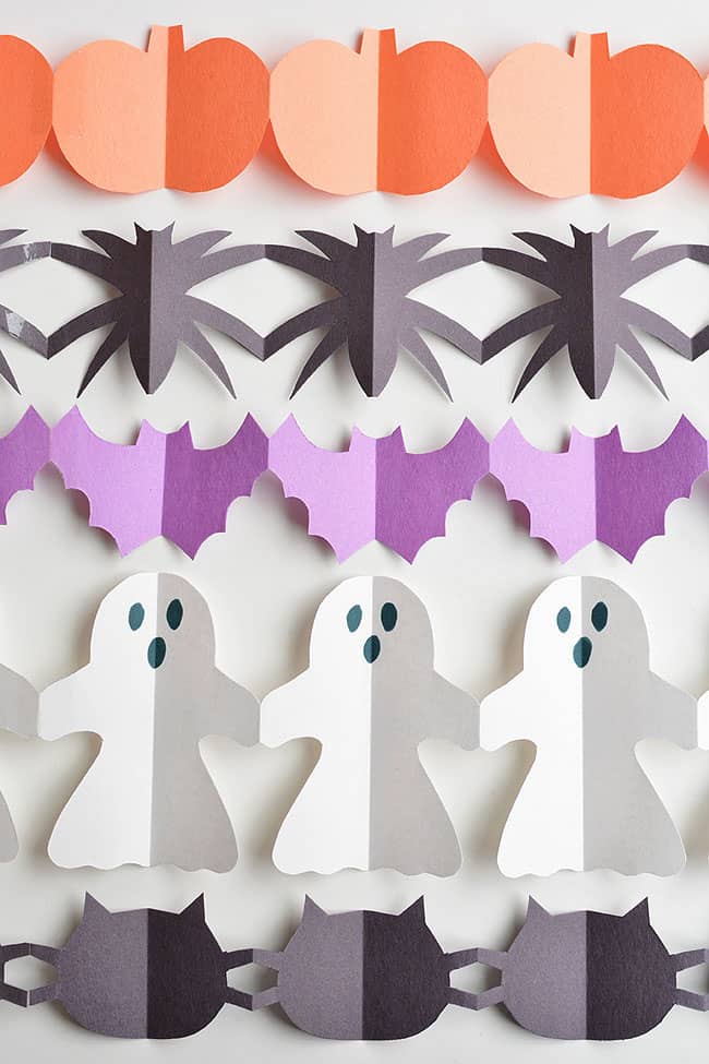 Orange pumpkins, black spiders, purple bats, white ghosts and black cats arranged as connected paper Halloween garlands