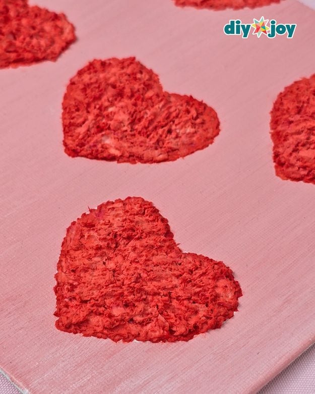 A raised textured heart painted on canvas using a tissue paper technique, an easy handmade wall art craft to sell