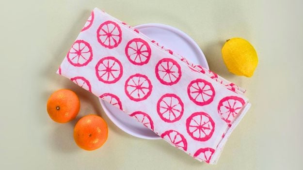 A cotton tea towel stamped in a repeat citrus print using a sliced lemon and fabric paint, a kitchen craft that sells in sets