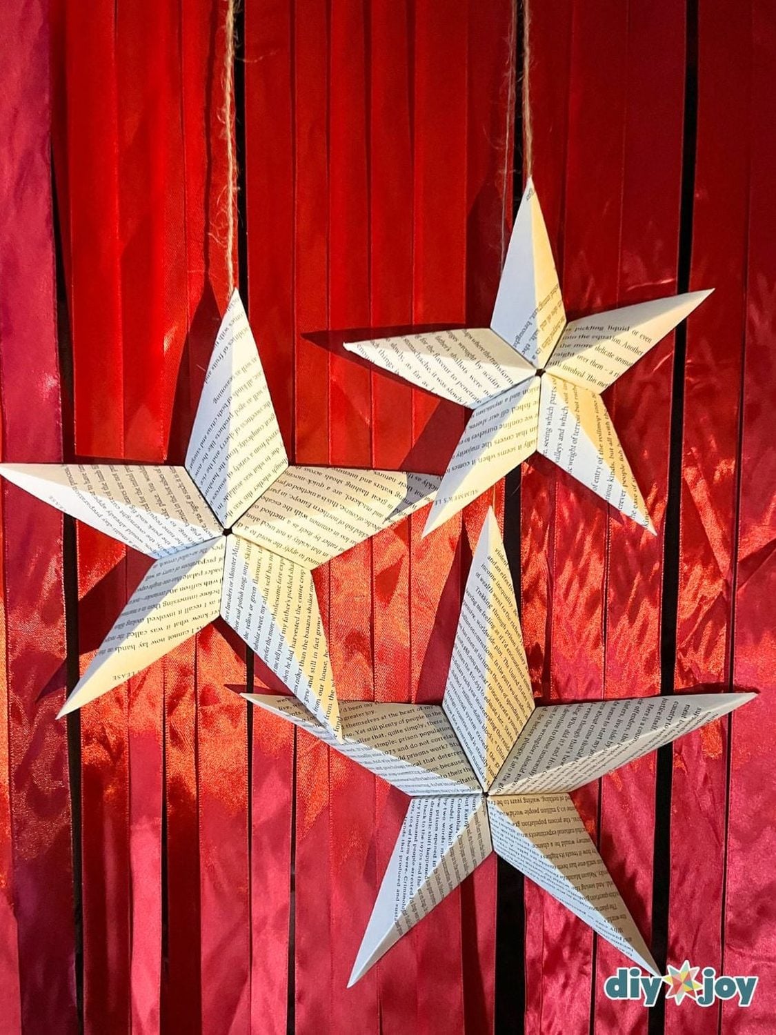 Three-dimensional stars folded from printed book pages hanging on twine in a window with soft light behind them