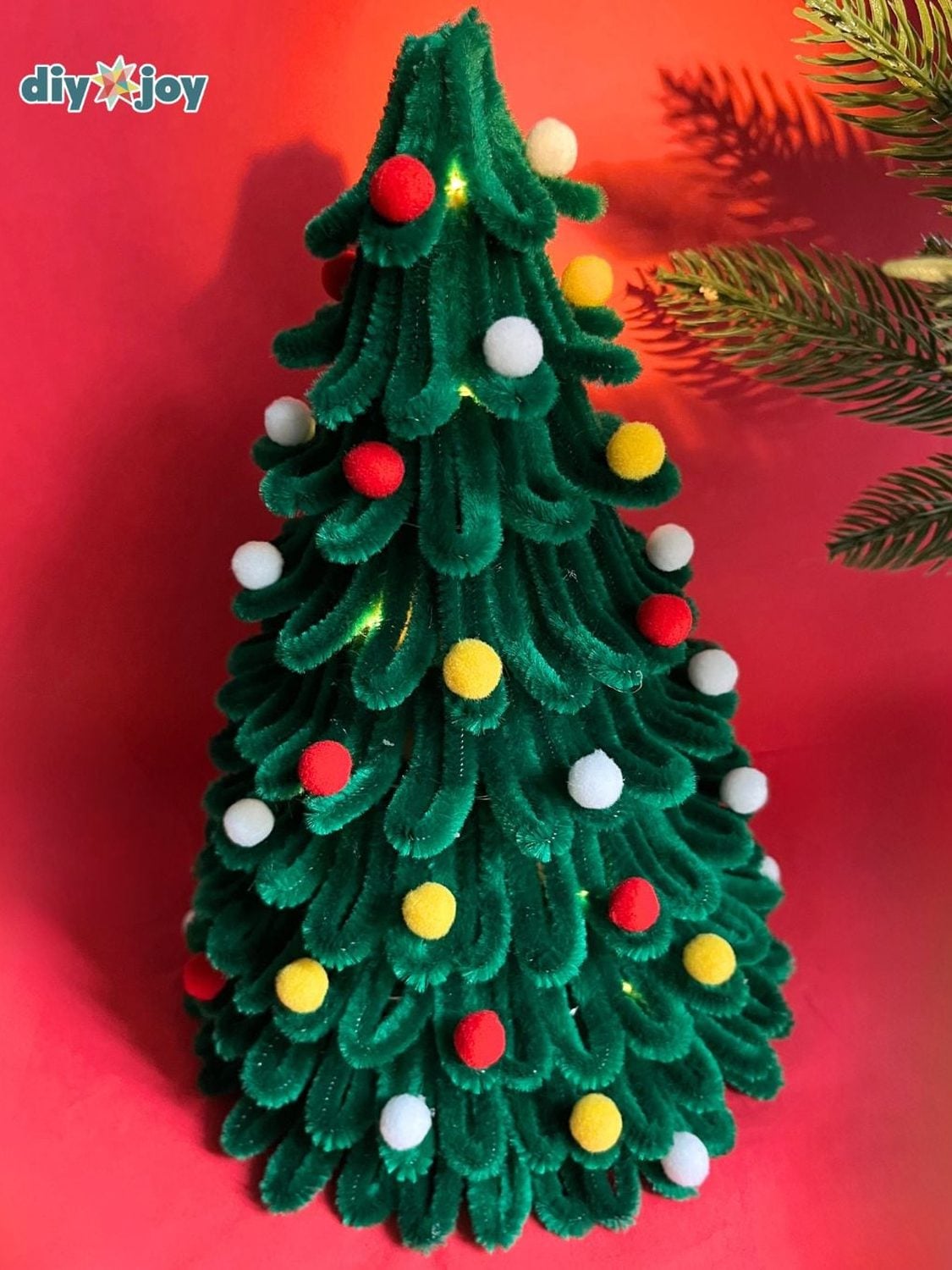 Tabletop Christmas tree made of looped green pipe cleaners on a cone, dotted with red, yellow and white mini pom poms