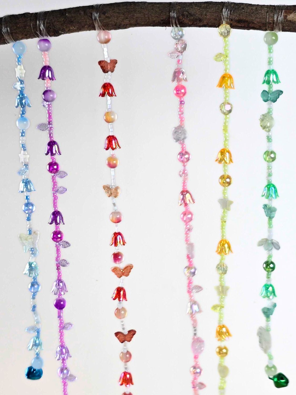 A handmade wind chime of mixed glass beads, silver charms and tiny bells hanging on strings from a ring outdoors
