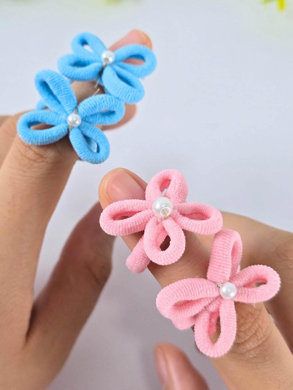 Several thin elastic hair tie rings topped with pearls, beads and tiny charms in pastel colors arranged on a white surface