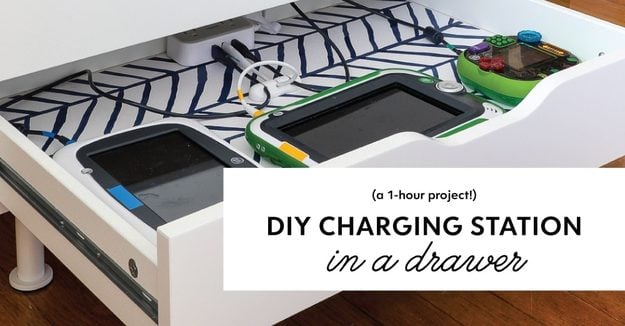 A power strip taped inside a lined dresser drawer with device cords routed through a drilled hole for a hidden charging station