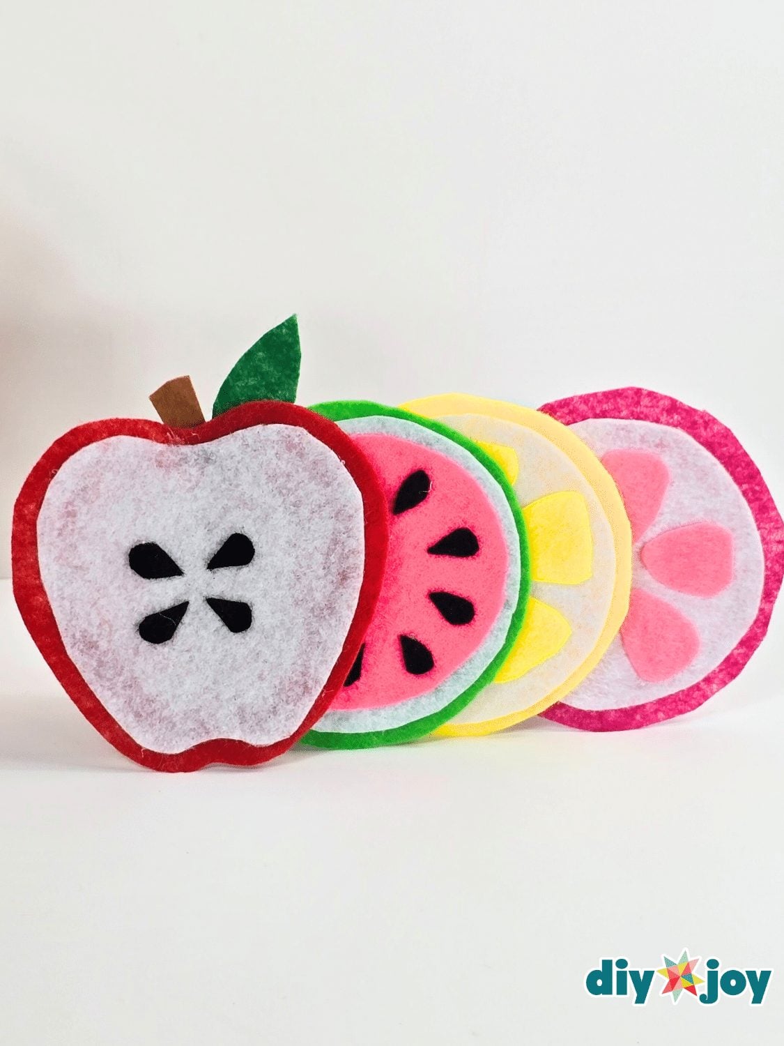 Four no sew felt coasters shaped like an apple, a watermelon slice, a lemon round and a dragon fruit slice on white