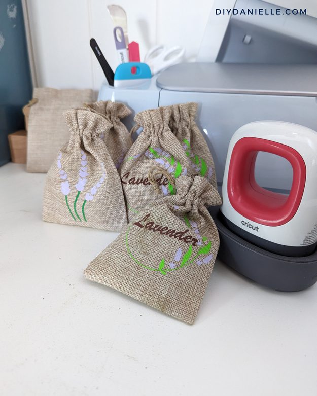DIY burlap project, four small burlap drawstring gift bags with iron on lavender sprig designs beside a heat press