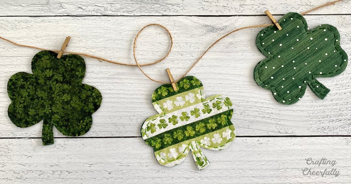 St Patricks Day decor, three green fabric shamrocks pegged to twine with wooden clothespins on white wood