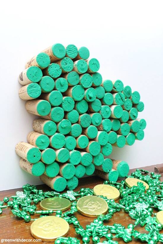 St. Patrick's Day decor, a shamrock made from wine corks with the cork tops painted green, propped against a wall beside gold coins