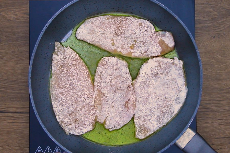 Four floured chicken cutlets pan frying in olive oil in a skillet for an easy chicken piccata dinner