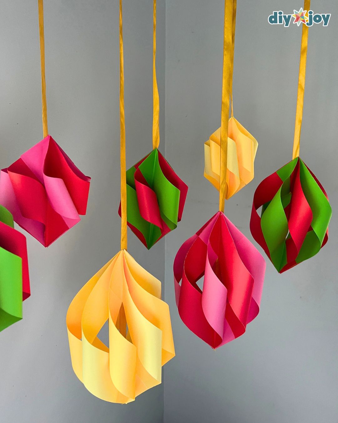 Yellow, pink and red-and-green paper ornaments on gold ribbon, a simple DIY Christmas decor project to make with kids