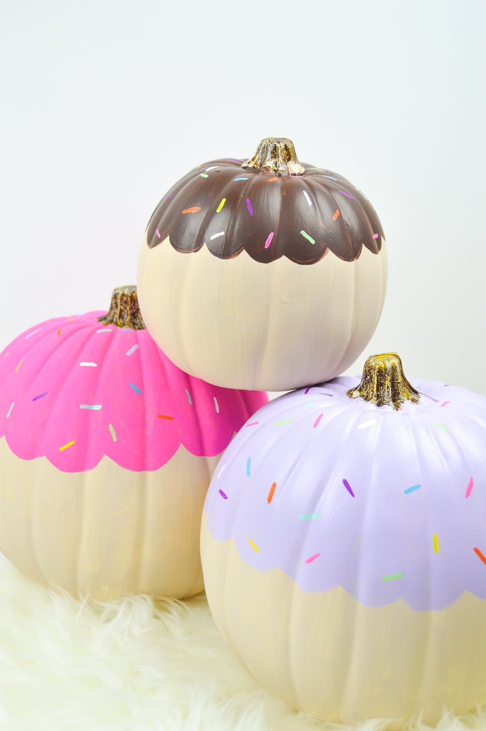 Three cream-painted pumpkins with painted brown, pink and lavender frosting bands plus colorful painted sprinkles