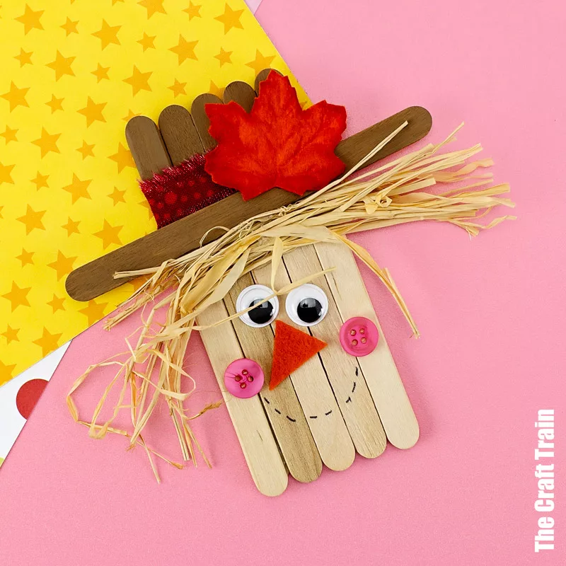 Craft Stick Scarecrow Fall Craft Fall craft for kids, a scarecrow made from craft sticks with googly eyes, a felt nose and a straw hat