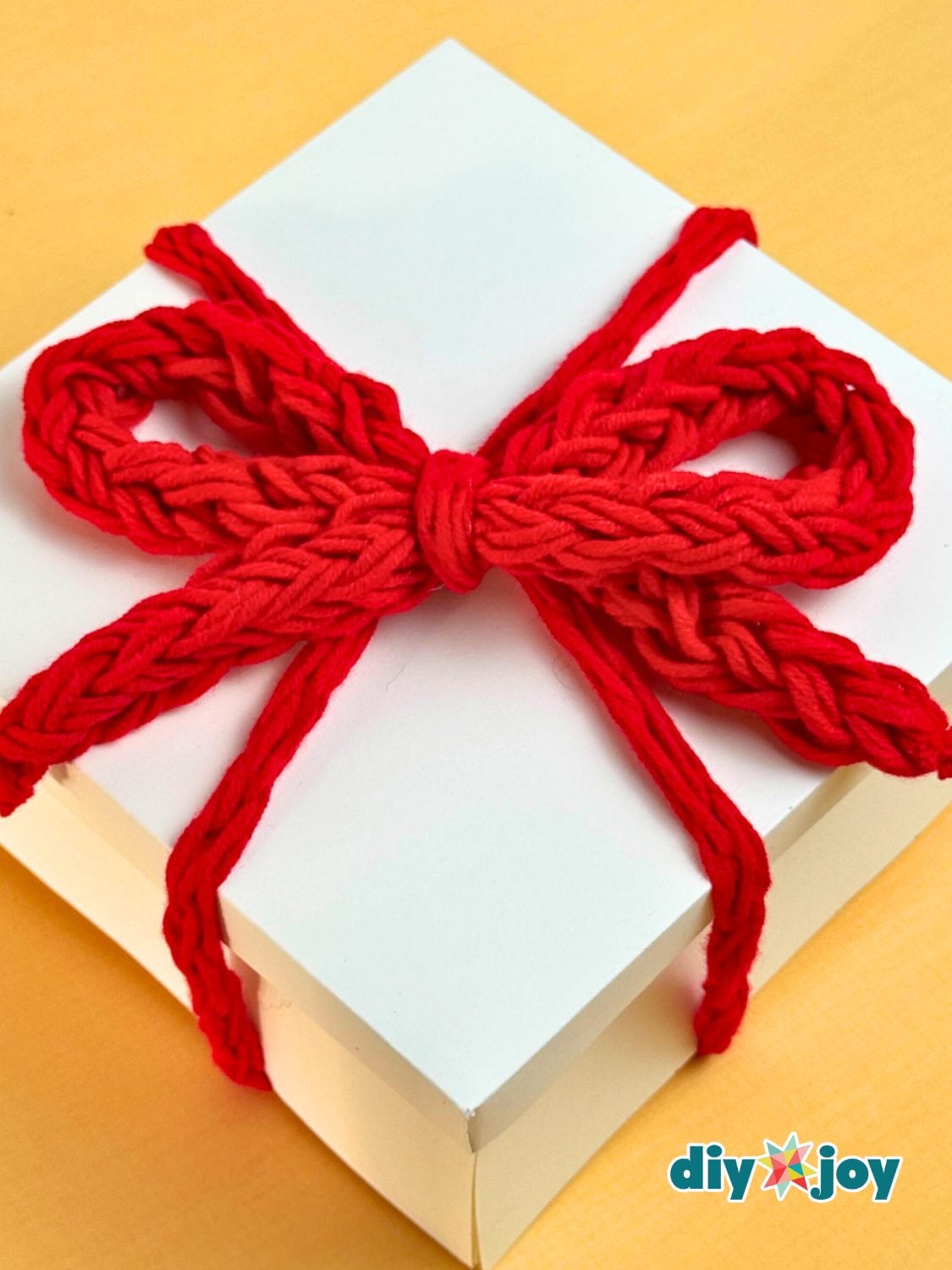 Finger Crochet Yarn Bow Topper A soft bow finger crocheted from leftover cream yarn, sitting on a wrapped parcel as a no hook topper
