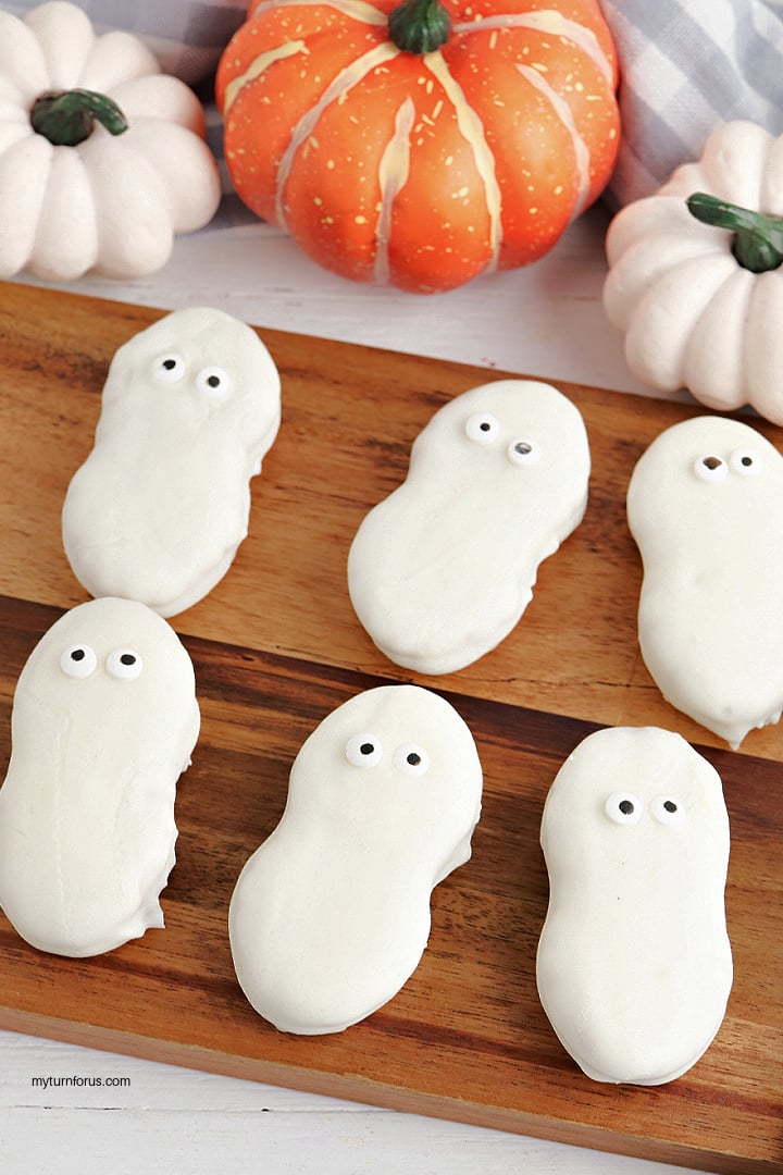 No-Bake Nutter Butter Ghost Cookies White chocolate covered Nutter Butter ghost cookies with small candy eyes arranged on a wooden serving board