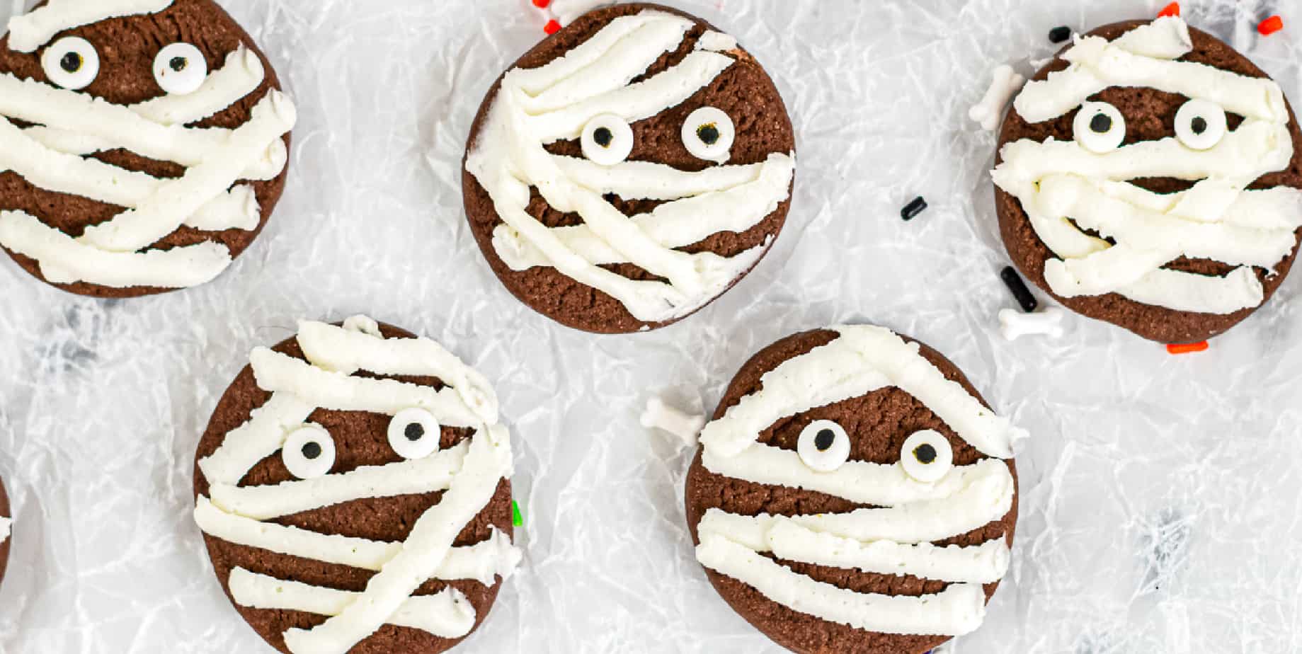 Mini Chocolate Mummy Cookie Treats Small chocolate mummy cookies with white icing bandages and candy eyes arranged on a serving plate for Halloween