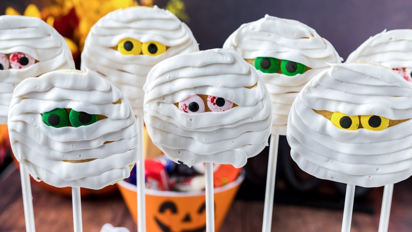 Easy Halloween Mummy Cookie Pops Round mummy cookie pops wrapped in white icing bandages with candy eyes and lollipop sticks for Halloween