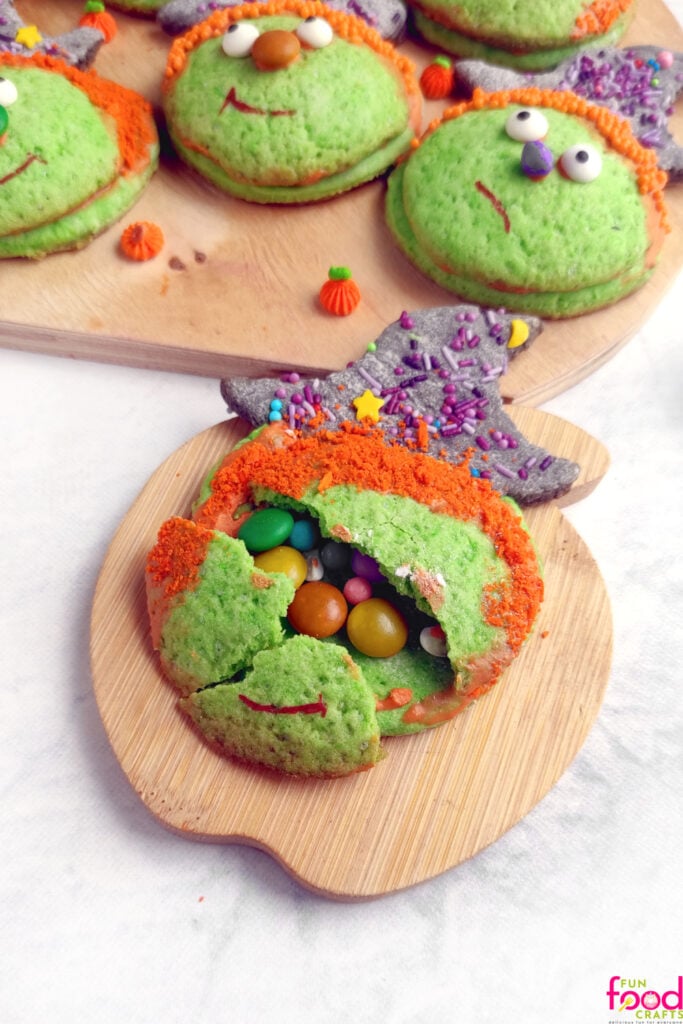 Witch Halloween Piñata Cookies Layered witch piñata cookies with one opened to reveal colorful candy hidden inside on a Halloween serving plate