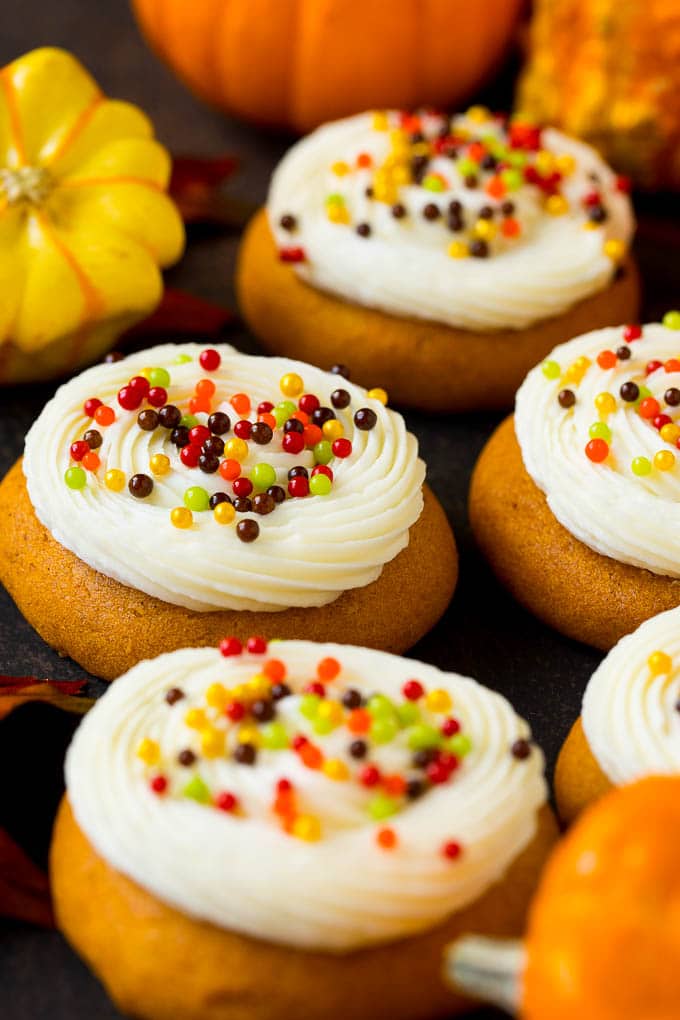 Frosted Pumpkin Cookies for Halloween Soft pumpkin cookies topped with piped cream cheese frosting and fall sprinkles beside small pumpkins