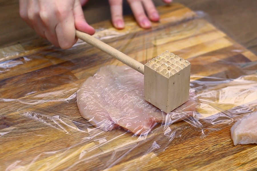 How to Make Chicken Piccata, pounding a butterflied chicken breast under plastic wrap to an even thickness with a mallet