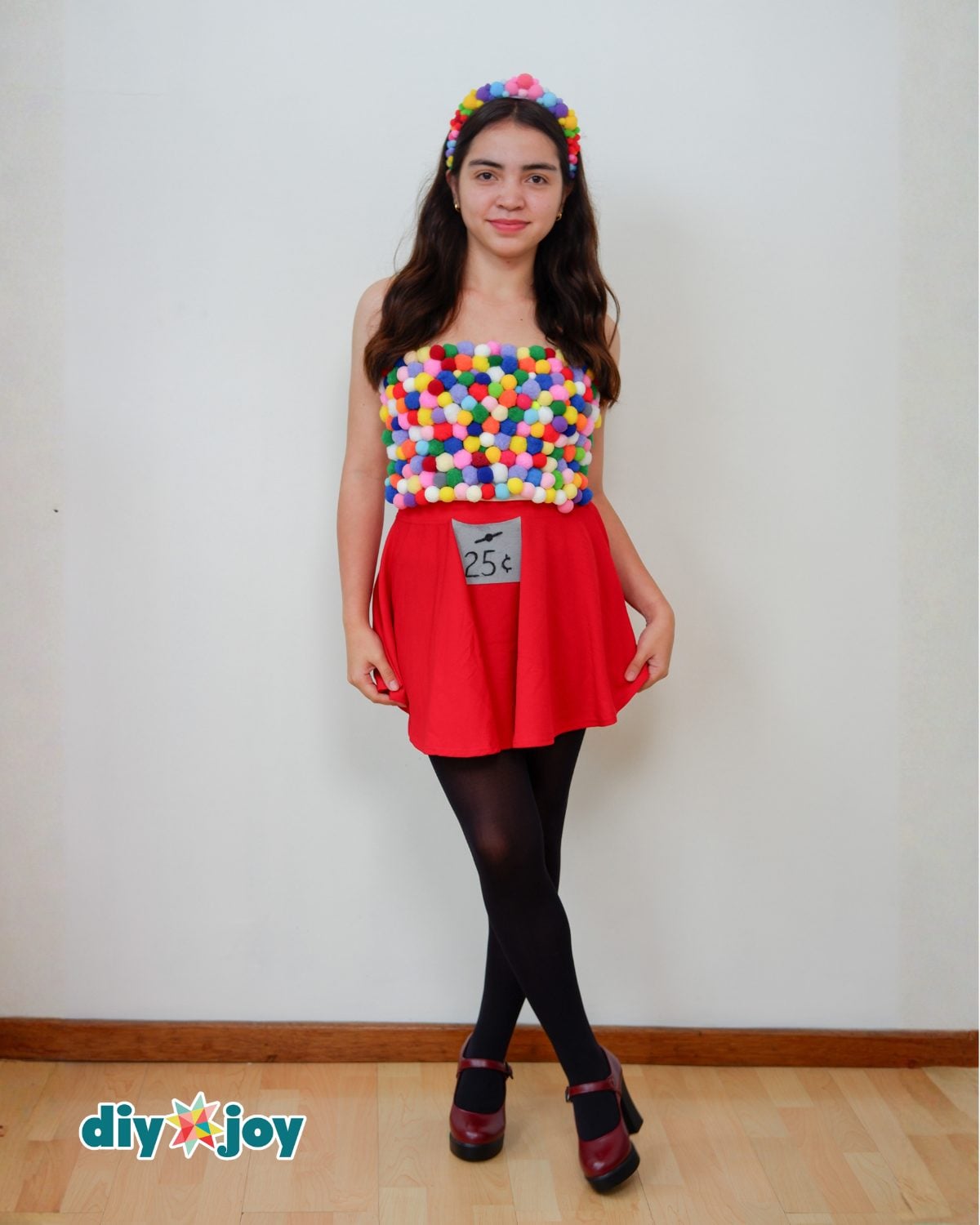 DIY Gumball Machine Halloween Costume Adult wearing a colorful pom-pom gumball machine costume with red skirt, coin label and matching pom-pom headband