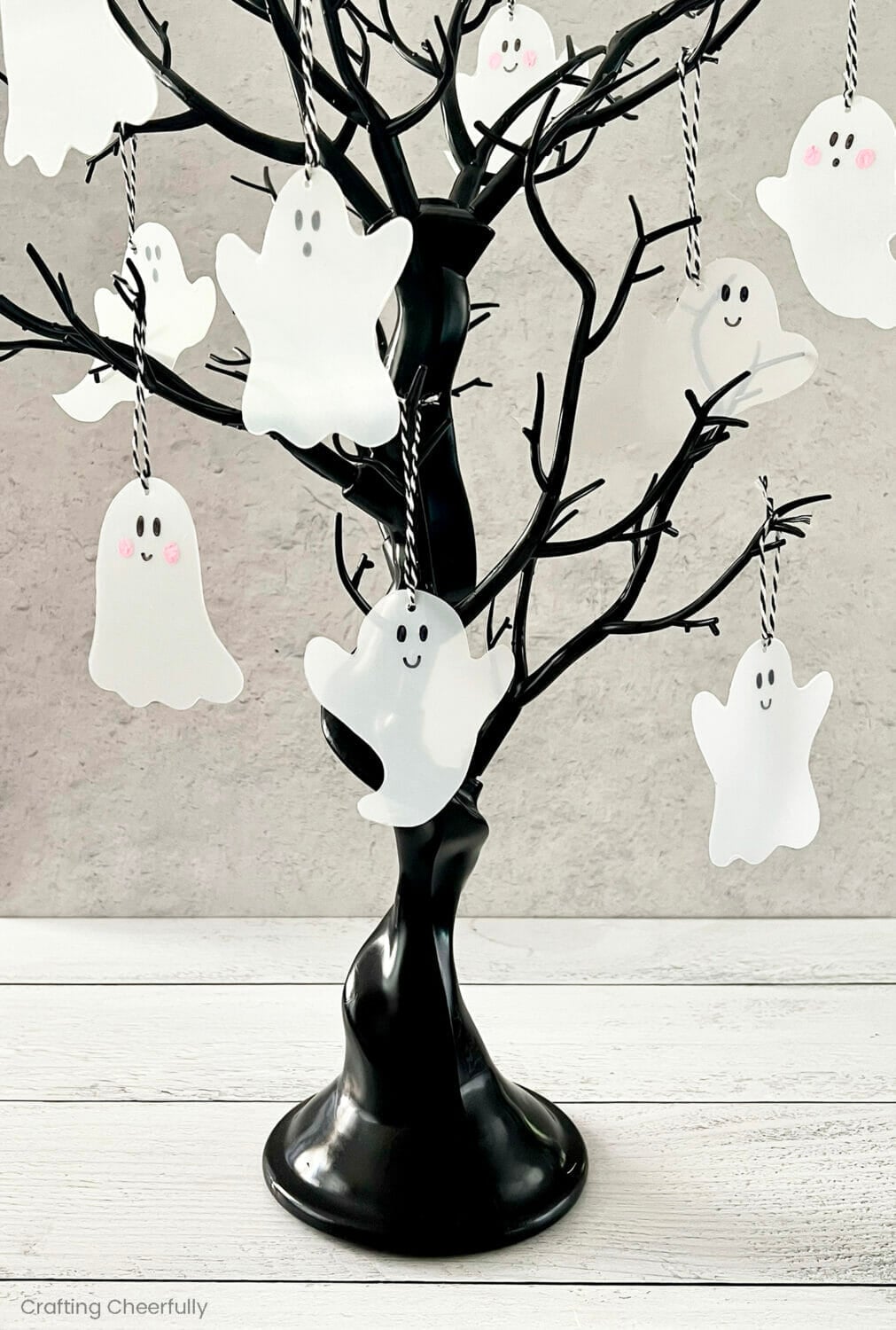 White craft-plastic ghost ornaments with marker faces and twine hangers displayed on a glossy black tabletop tree