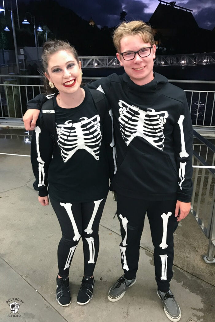 DIY Skeleton Iron-On Halloween Costumes Two teens wearing black skeleton costumes with white iron-on bones outdoors and Polka Dot Chair source mark