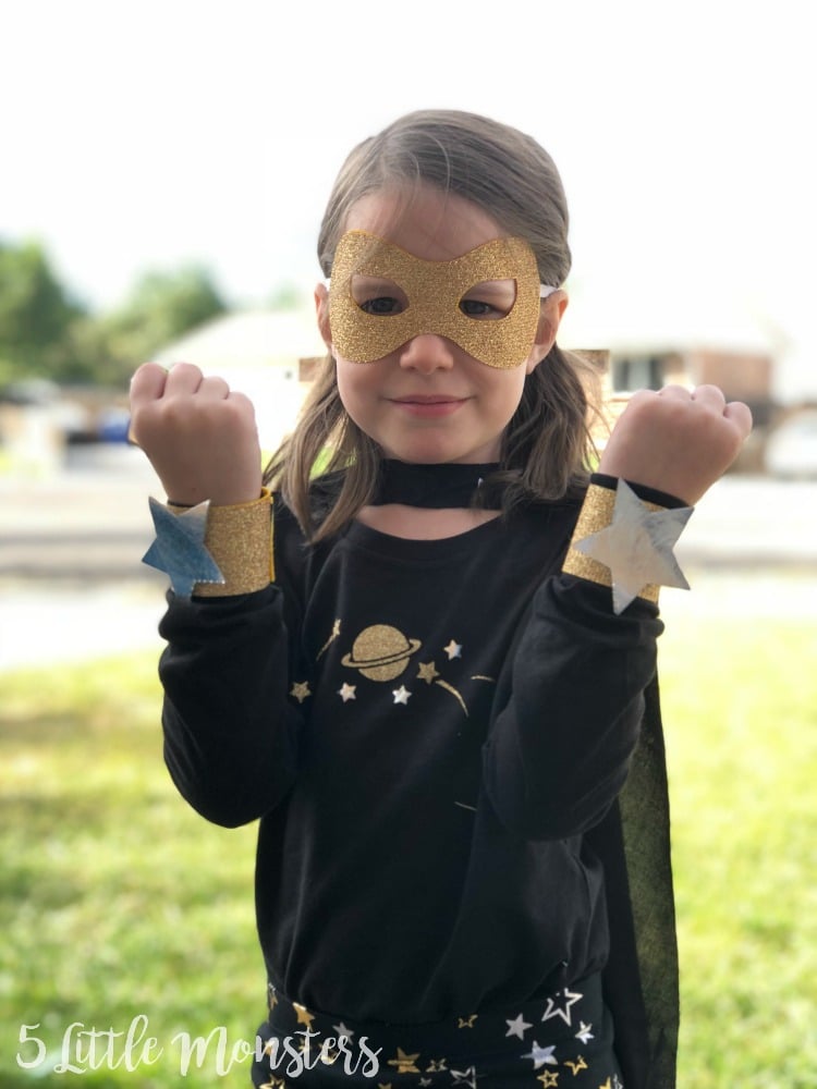 DIY Galaxy Girl Superhero Costume Child wearing a Galaxy Girl superhero costume with a glitter mask, star cuffs, black shirt and matching cape