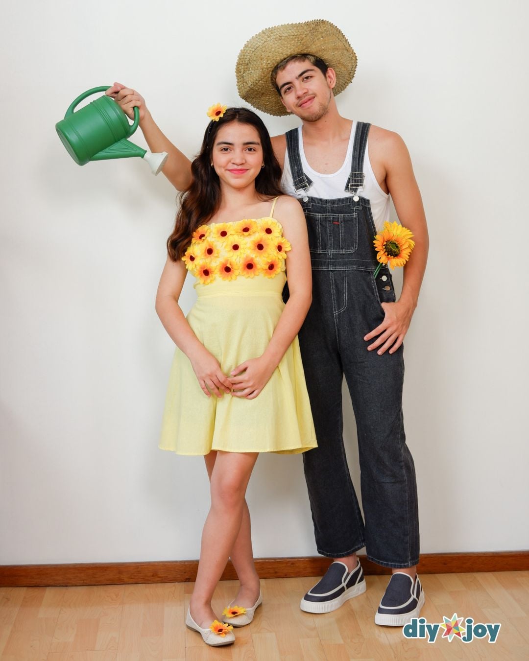 Sunflower and Gardener Halloween Costume Two adults in sunflower and gardener costumes with flowered yellow dress, denim overalls, straw hat and watering can