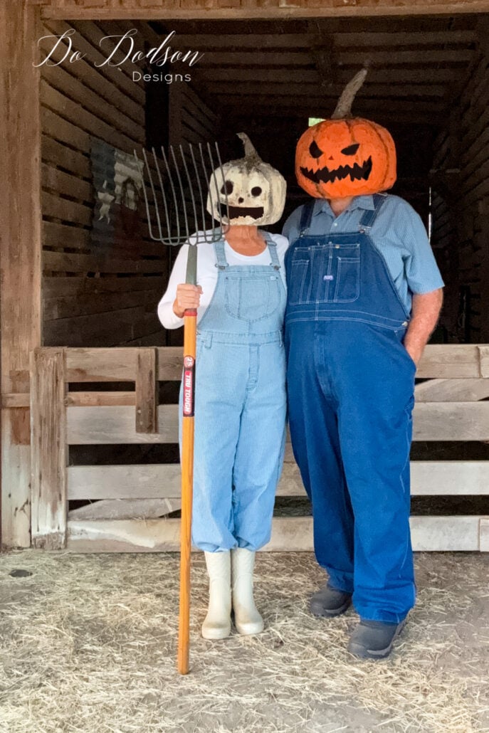 Paper Mache Pumpkin Head Costume Two adults wearing full costumes with orange and pale paper mache pumpkin heads in front of a rustic barn