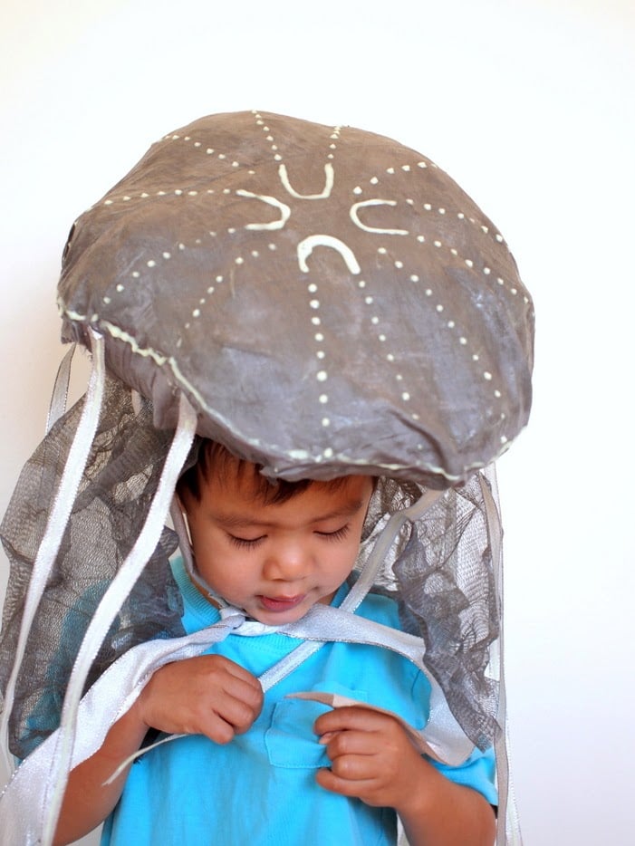 Glow-in-the-Dark Jellyfish Costume Child wearing a glow-in-the-dark jellyfish hat with a bubble-wrap dome, painted details, mesh and silver ribbons