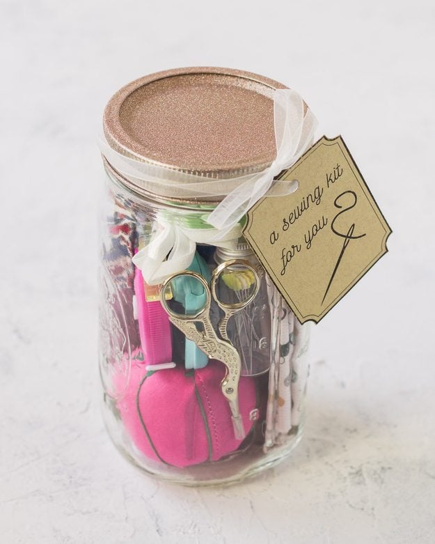Mason jar sewing kit with a pink pincushion, embroidery scissors and folded fabric inside, a glitter lid and a sewing kit for you gift tag