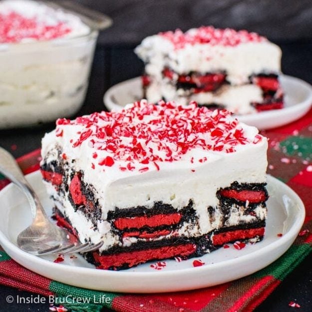 Square slice of peppermint Oreo icebox cake with red filled cookie layers, white no bake cheesecake and crushed candy cane on top